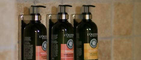 Three L'OCCITANE shower bottles mounted on a tiled wall.