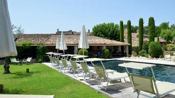 A poolside area with lounge chairs and umbrellas, a clear sky, and a building with a tiled roof in the background.
