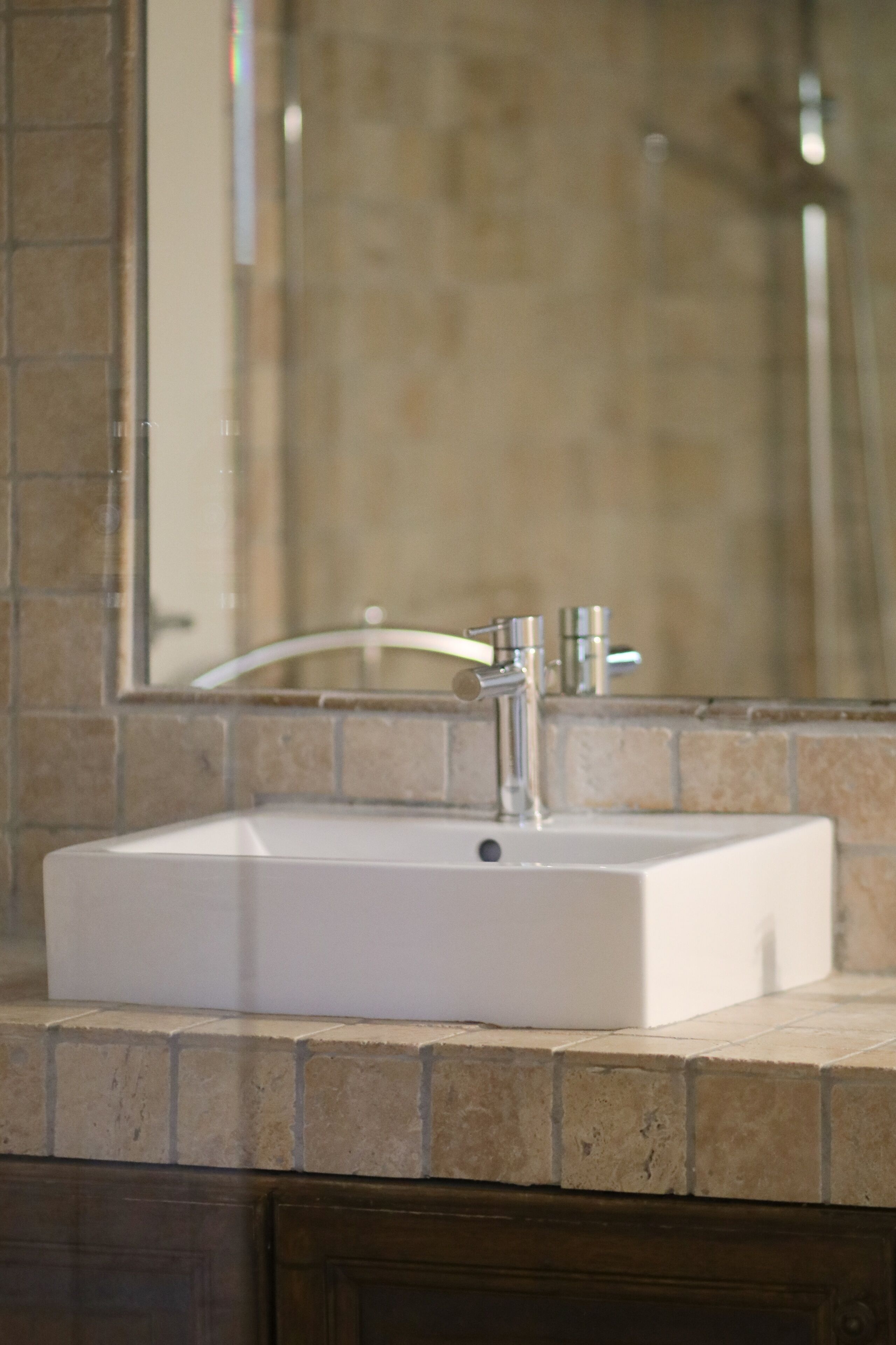 Une salle de bain avec un lavabo blanc, un miroir et un mur recouvert de carreaux.