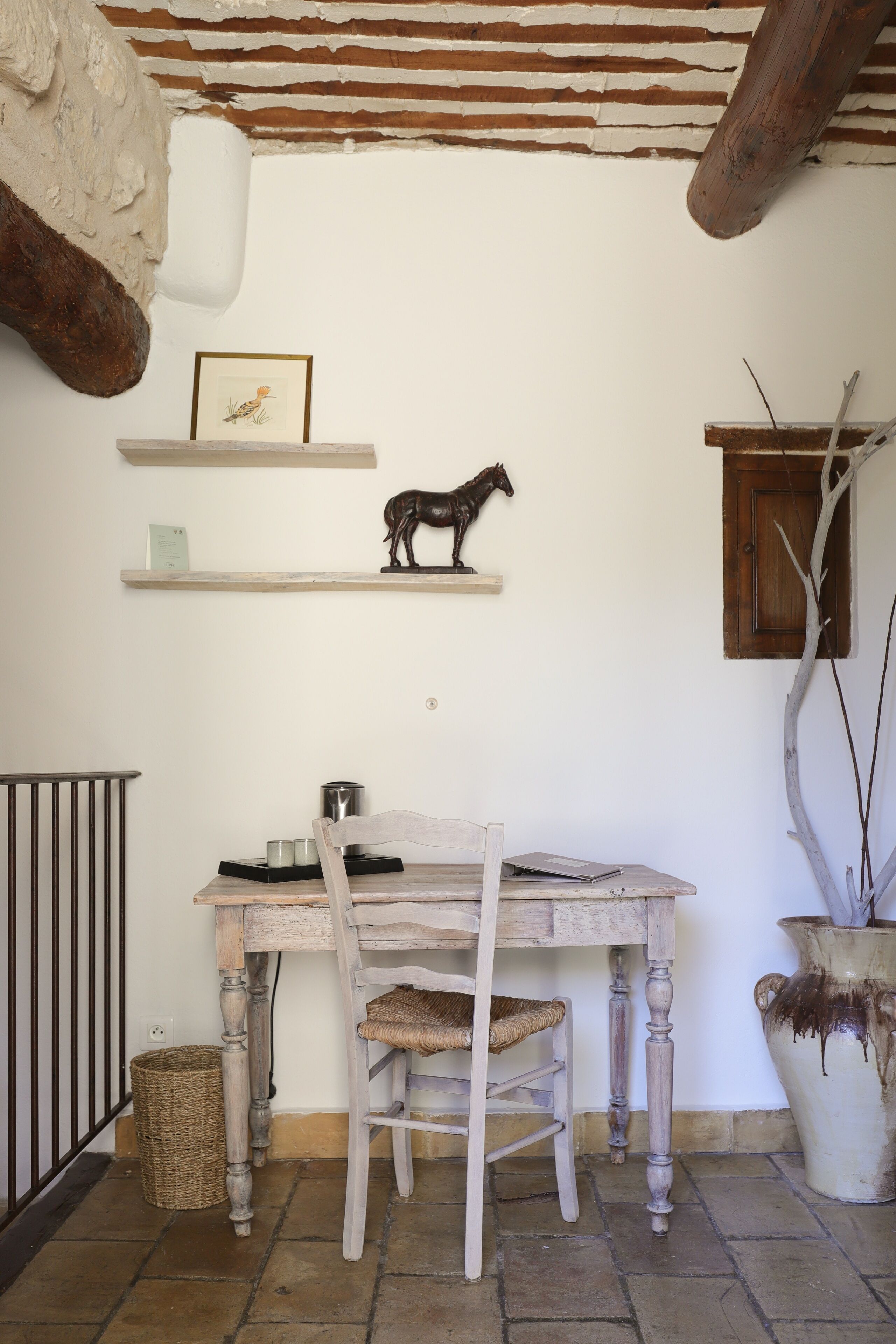 A rustic dining area with a wooden table, chairs, and a vase. There are shelves with a framed picture and a horse sculpture.