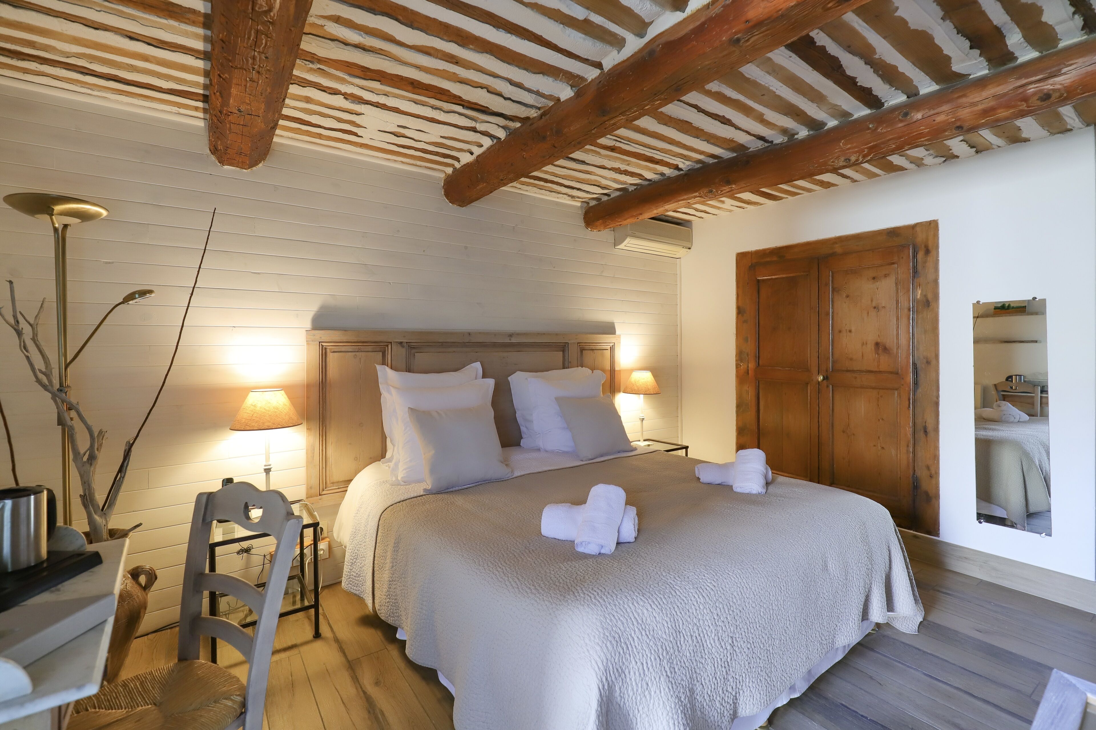 Een slaapkamer met een houten plafond, een bed met wit beddengoed, een nachtkastje met een lamp en een houten garderobe.
