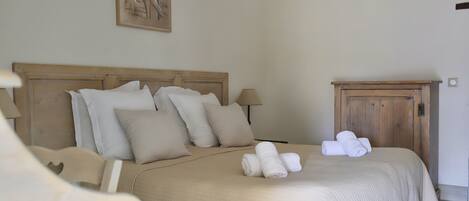 A neatly made bed with white linens and towels, a wooden headboard, and a painting on the wall.