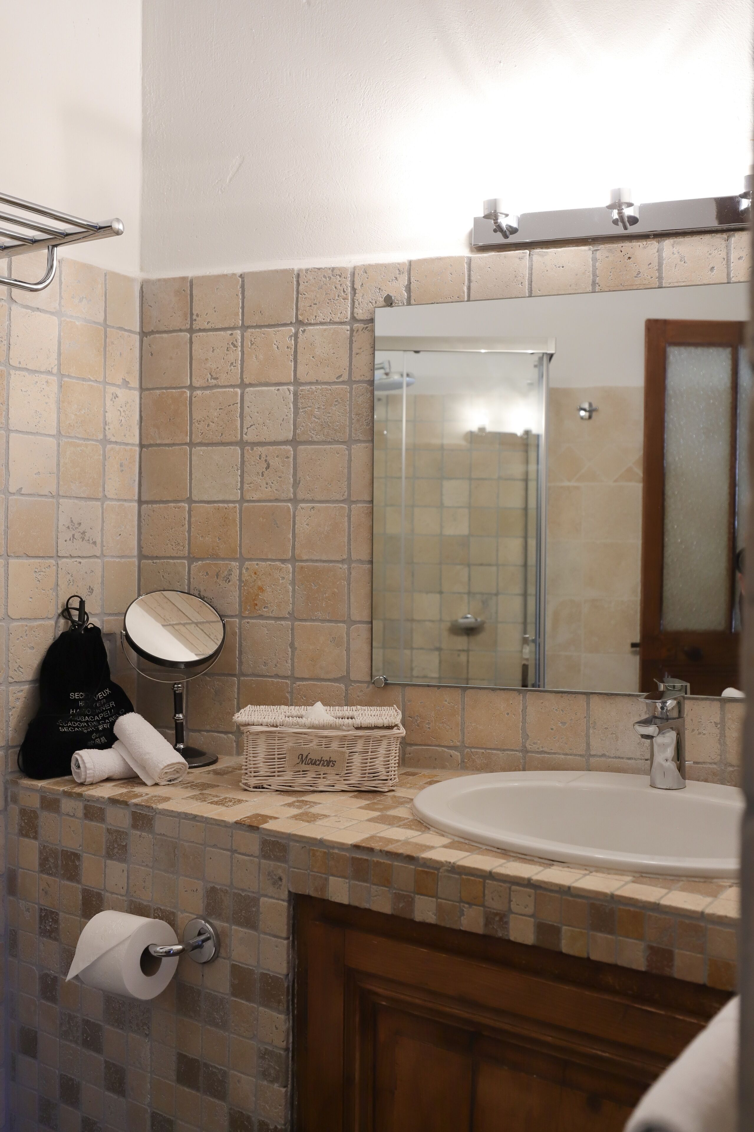 Une salle de bain avec un mur recouvert de carreaux derrière le lavabo, un lavabo, un miroir, un porte-serviettes et un porte-rouleau de papier toilette.