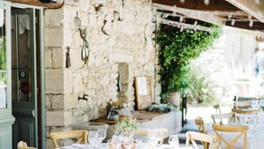 Un área de comedor al aire libre con muros de piedra, sillas de madera y mesas preparadas para una comida.