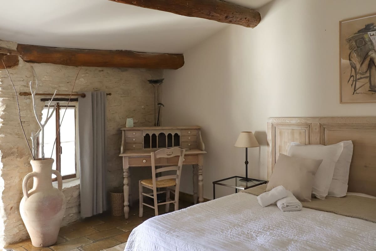 Une chambre confortable avec un grand lit, un bureau en bois et un vase décoré de branches.