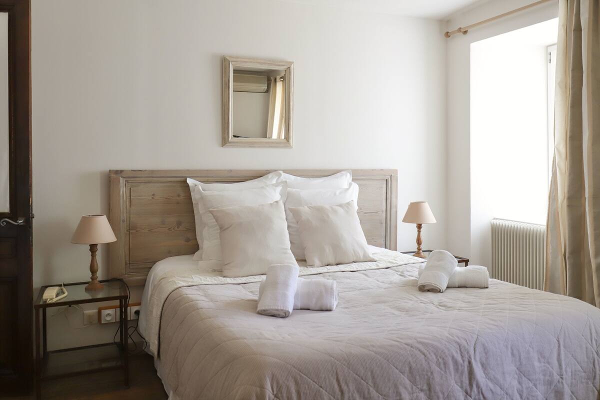 Un lit bien fait, avec des oreillers et des serviettes, une lampe de chevet et un miroir au mur.