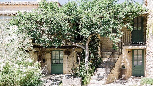 Un edificio de piedra con una puerta verde, una escalera y un árbol en primer plano.