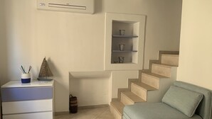 Een kamer met een trap, een bank, een bureau met lades en een wandplank met decoratieve objecten.