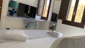 Een hotelkamer met een bed, een bureau met een computer en een televisie, een stoel en een raam met uitzicht.
