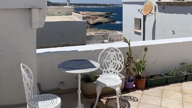 Een terras met een witte tafel en twee stoelen, met uitzicht op een rotsachtige kustlijn.
