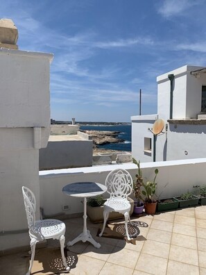Eine Terrasse mit einem weißen Tisch und zwei Stühlen mit Blick auf eine felsige Küstenlinie.