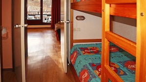 Ein Zimmer mit Etagenbetten, Holzboden, einer Tür zu einem Balkon und einem fenster mit Vorhängen.