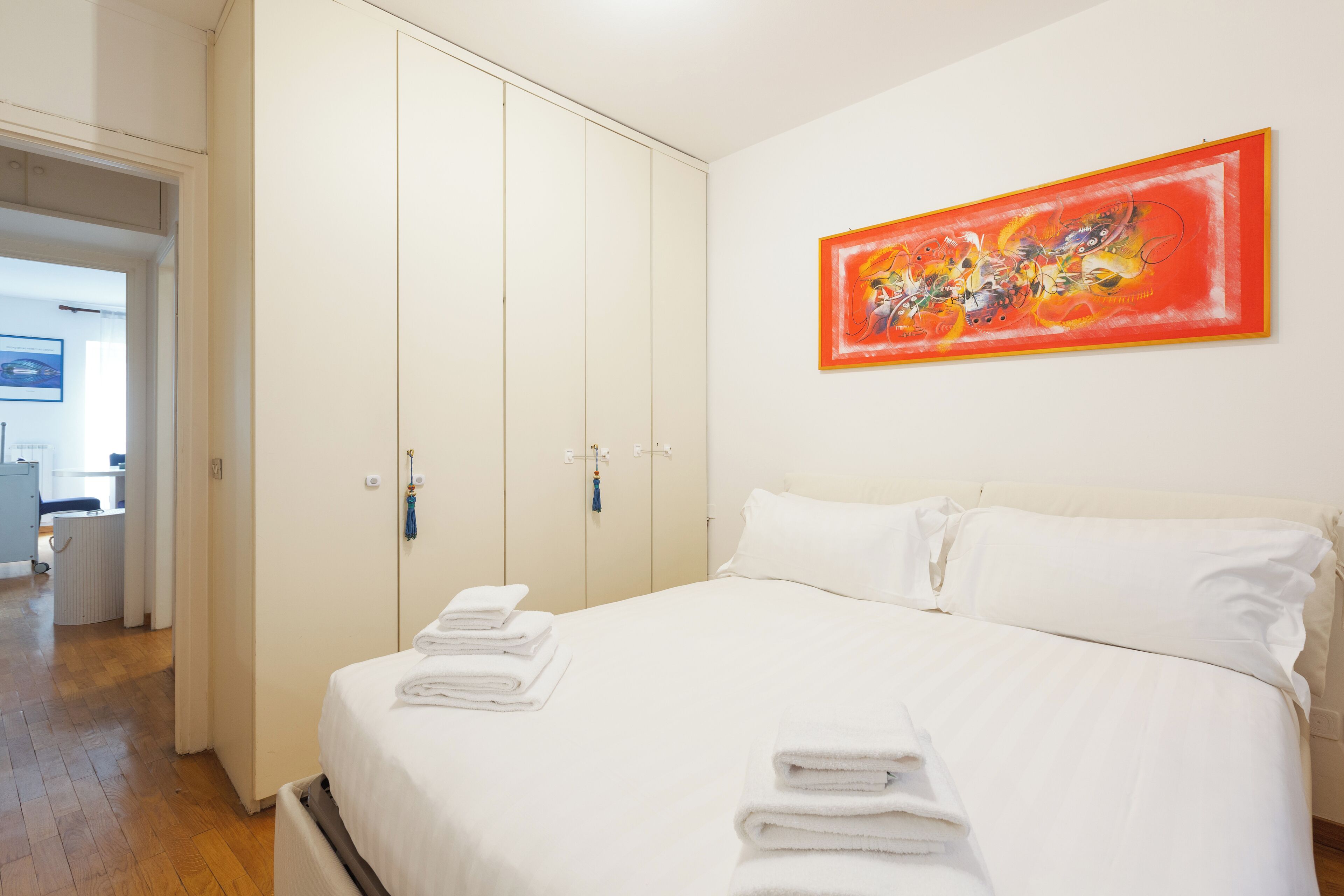 Une chambre d’hôtel avec un grand lit, du linge de lit blanc, une armoire et un tableau au mur.