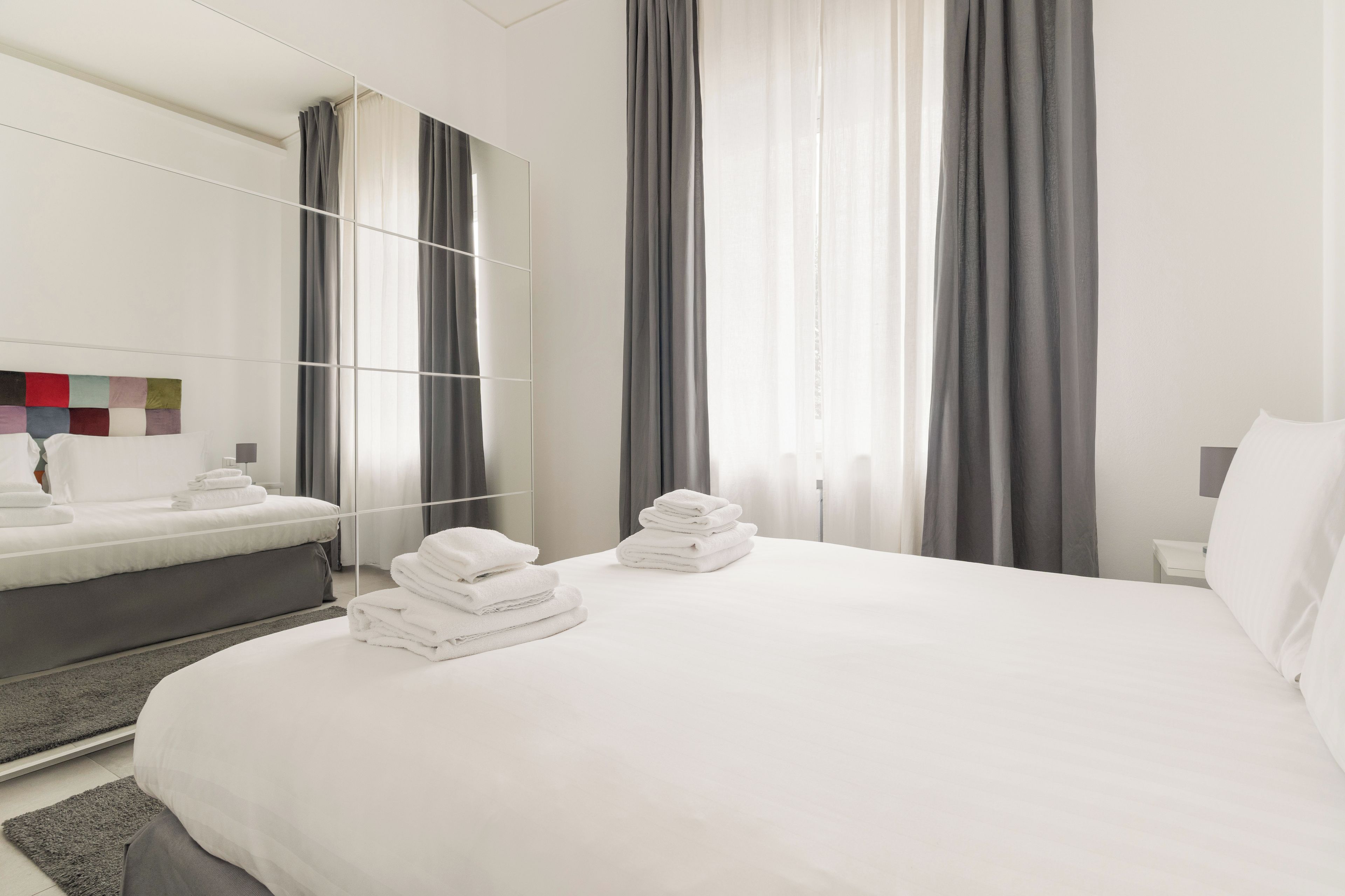 Een hotelkamer met een bed, nachtkastje, spiegel en een raam met gordijnen.