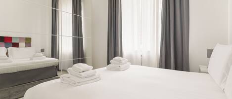 Een hotelkamer met een bed, nachtkastje, spiegel en een raam met gordijnen.