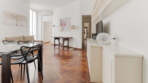 A modern living room with a glass dining table, black chairs, a white sofa, and a TV on a white cabinet. - Brera Apartments in San Marco (Milan)