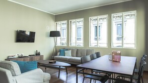 A modern living room with a sofa, coffee table, dining table, and a TV mounted on the wall. - Brera Apartments in San Marco (Milan)