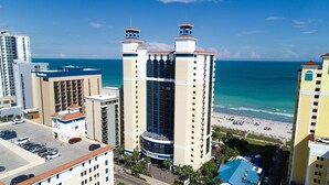 A high-rise hotel with a beach view, multiple balconies, and a parking area.
