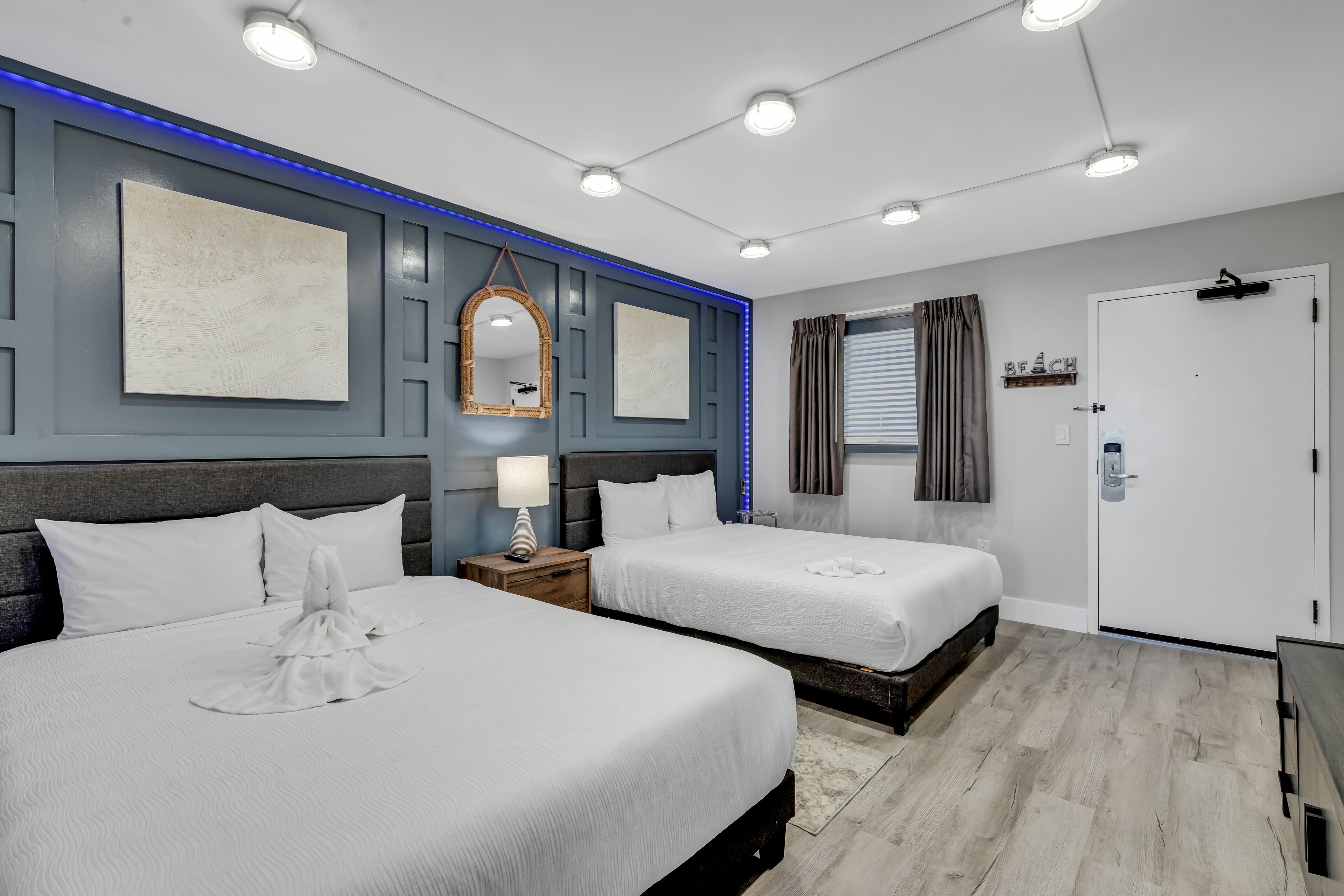 A hotel room with two beds, a large mirror, and a wall-mounted shelf with a 'BEACH' sign.