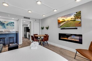 Uma sala de estar moderna com lareira, TV na parede e área de jantar com mesa e cadeiras.