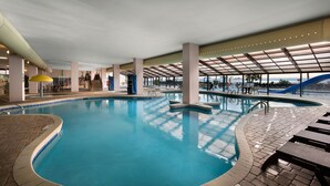 An indoor swimming pool with clear water, surrounded by lounge areas and a covered seating area.