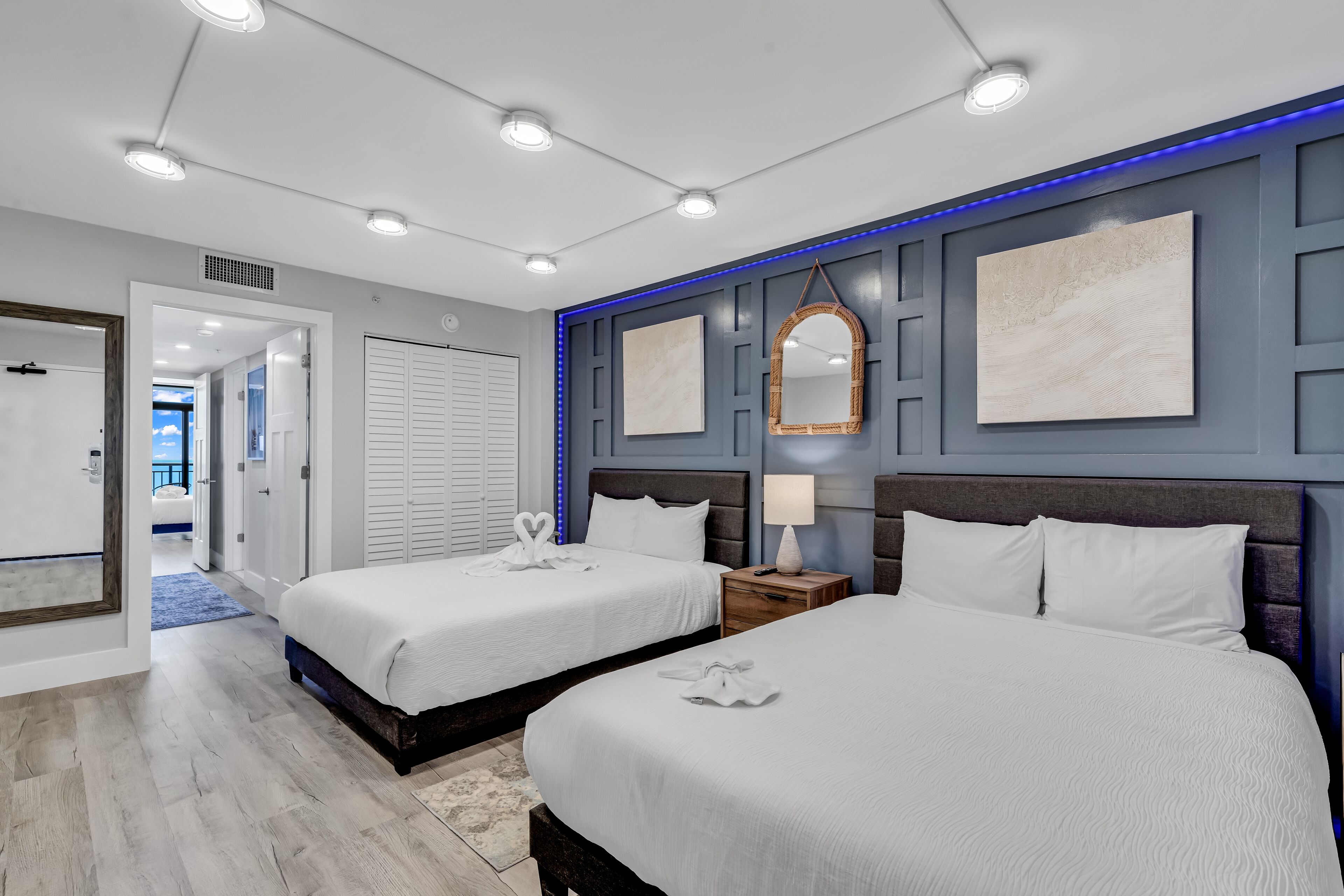 A hotel room with two beds, a large mirror, and a view of the sea.