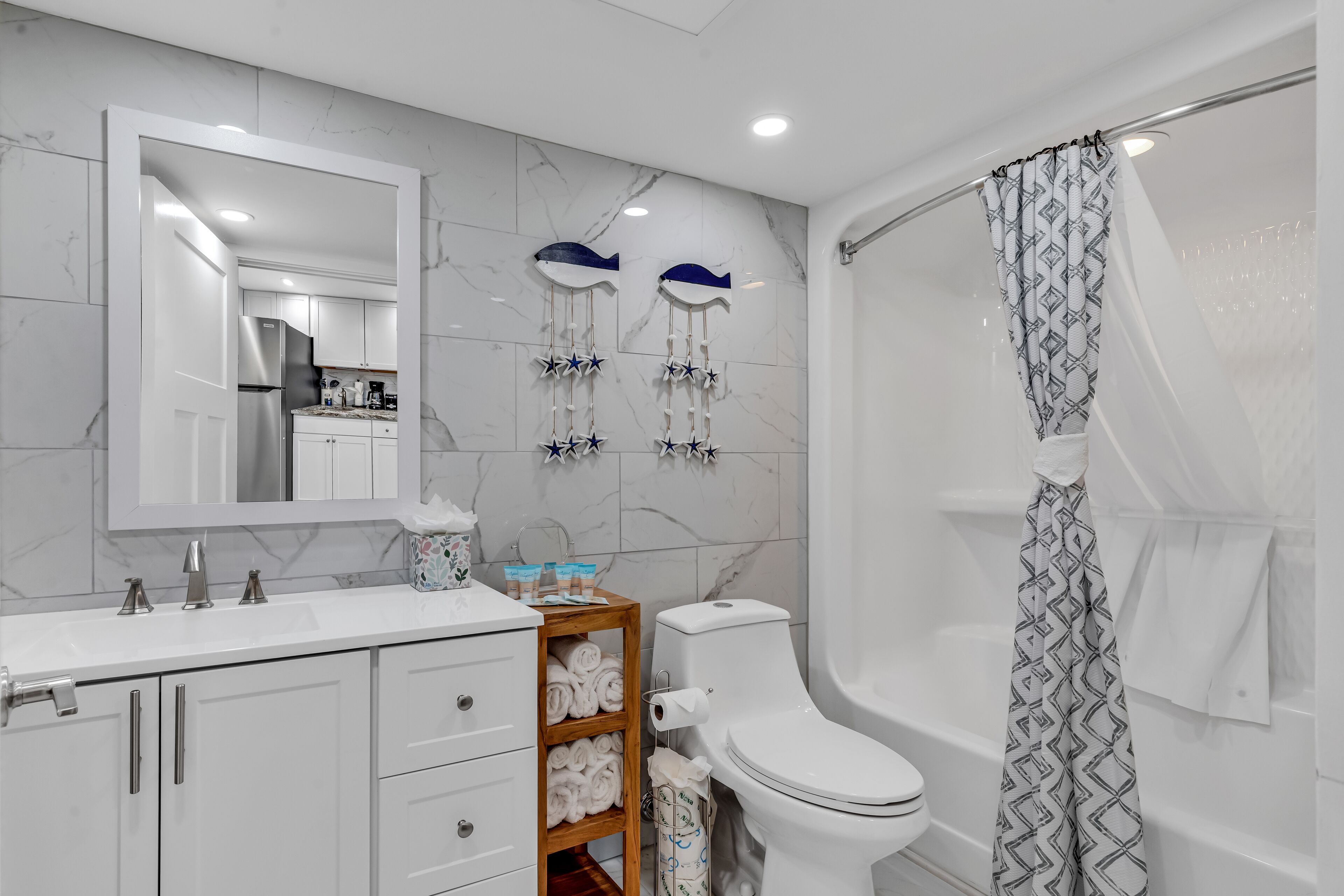 A modern bathroom with a white sink, mirror, and toilet. There are towels on a shelf, and a shower curtain with a geometric pattern.