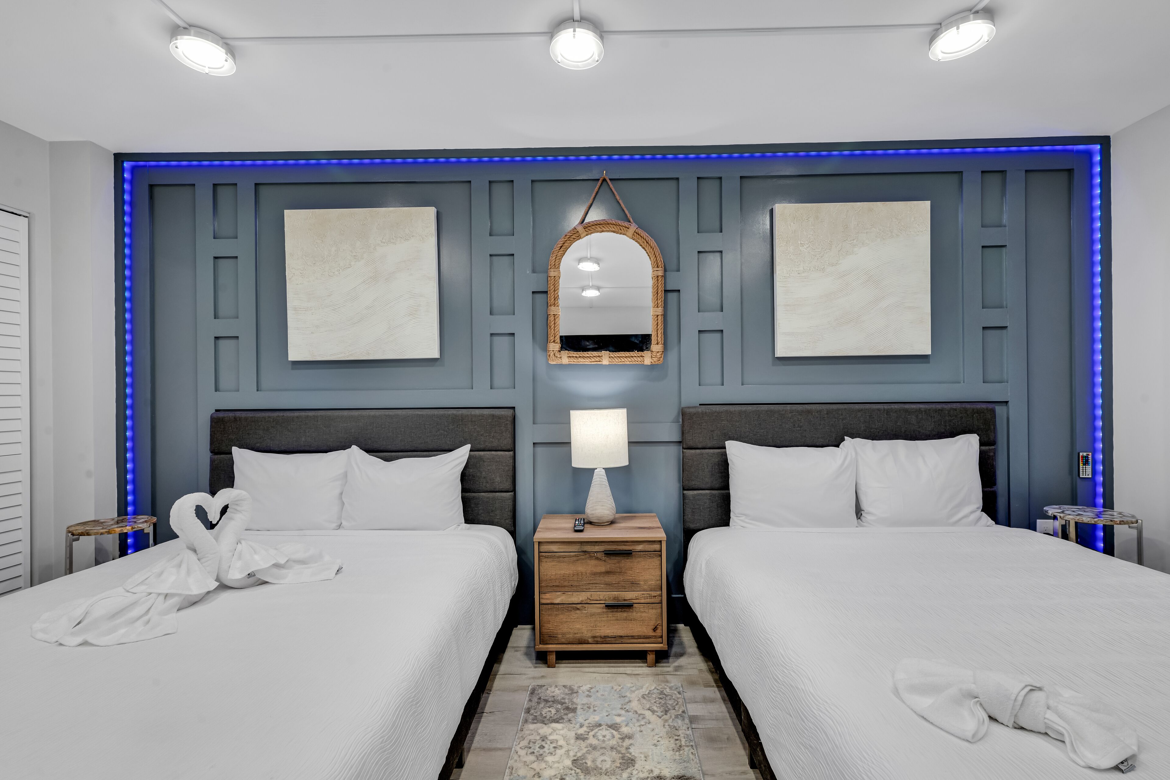 Une chambre d’hôtel avec deux lits, une table de chevet en bois, un miroir et une bande lumineuse à LED bleue.