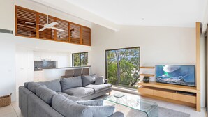 Una sala de estar moderna con un sofá seccional gris, una mesa de centro de vidrio y un televisor de pantalla plana grande sobre un mueble de televisión de madera.
