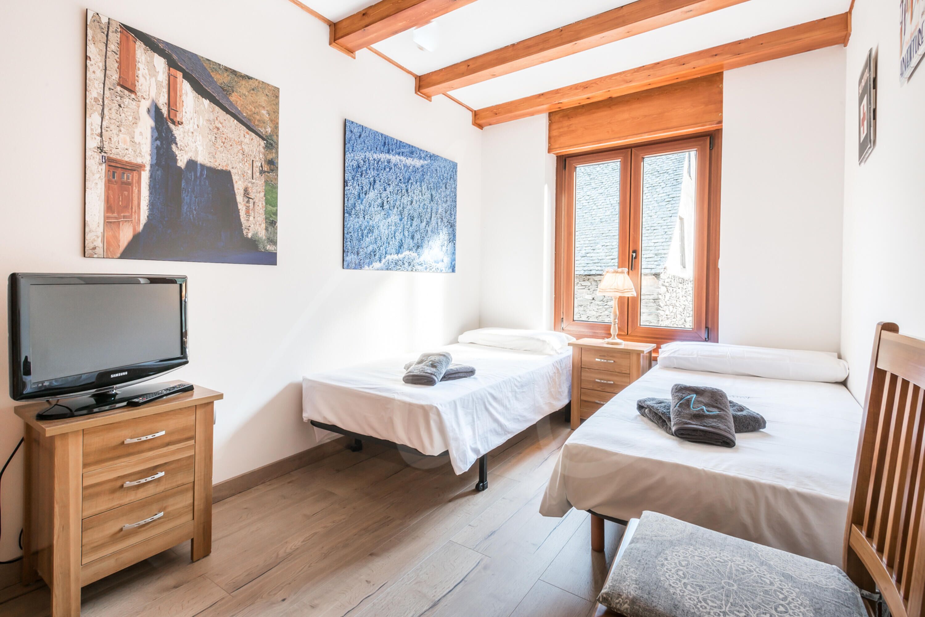A bedroom with two beds, a TV, wooden furniture, and artwork on the walls.