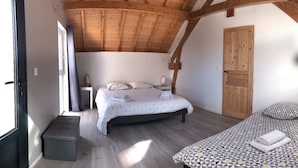 A bedroom with a sloped ceiling, a bed with a geometric-patterned bedspread, a bedside table with a lamp, and a wooden door. - Les Chambres du golf - Golf de La Chassagne (Malain)