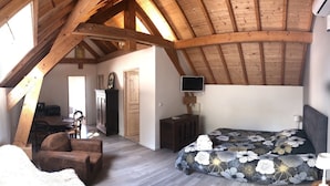 A bedroom with a wooden ceiling, a bed with a floral bedspread, a TV on the wall, and a chair. - Les Chambres du golf - Golf de La Chassagne (Malain)