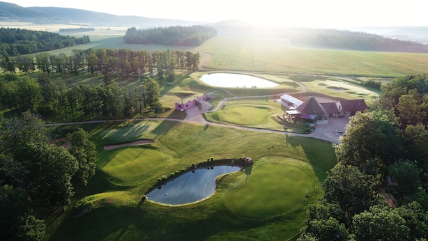 An aerial view of a golf course with a clubhouse, a pond, and surrounding wooded areas. - Les Chambres du golf - Golf de La Chassagne (Malain)