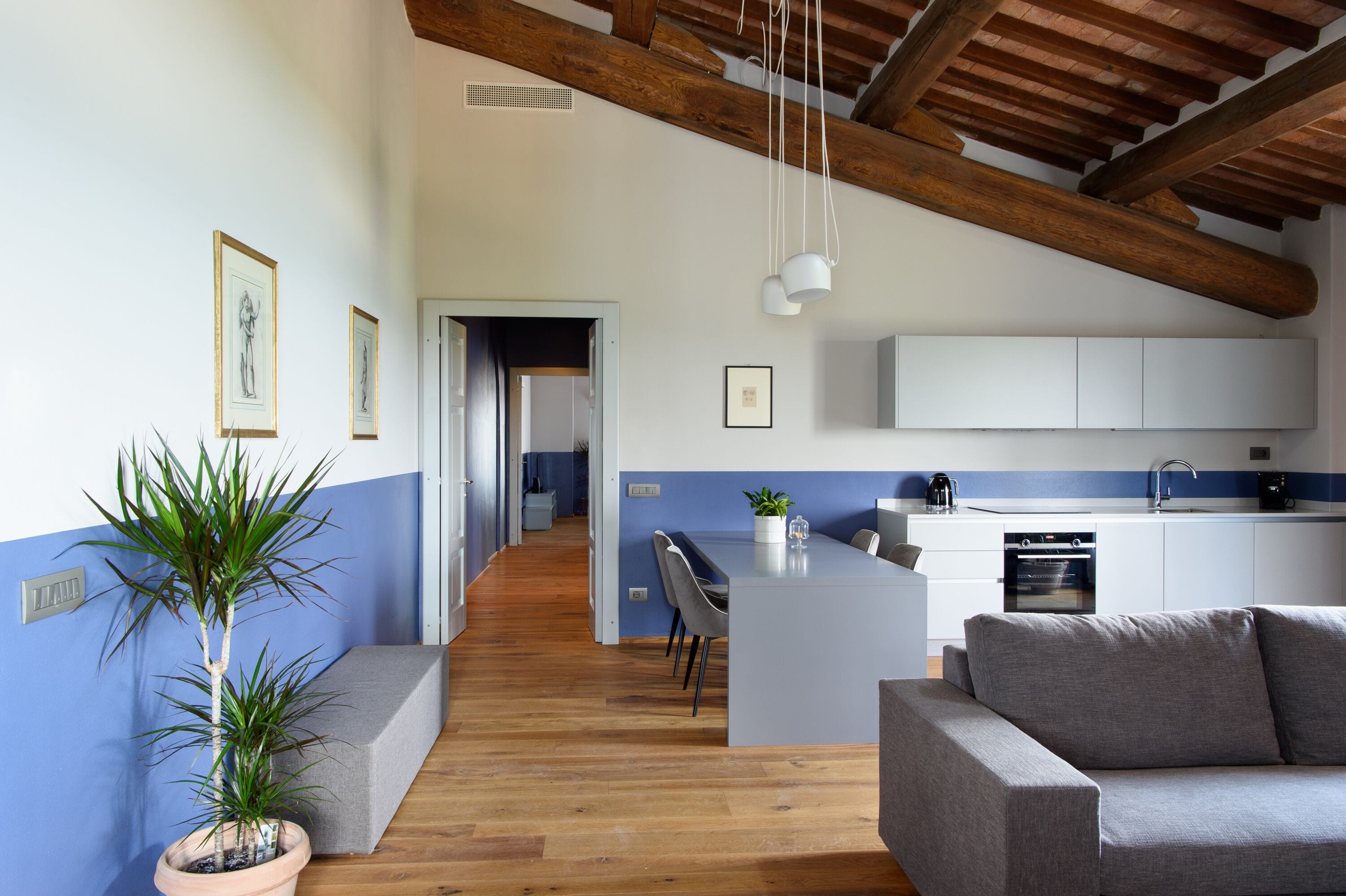 A modern kitchen with white cabinets, a grey sofa, and a wooden ceiling.