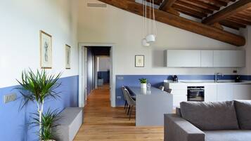 A modern kitchen with white cabinets, a grey sofa, and a wooden ceiling.