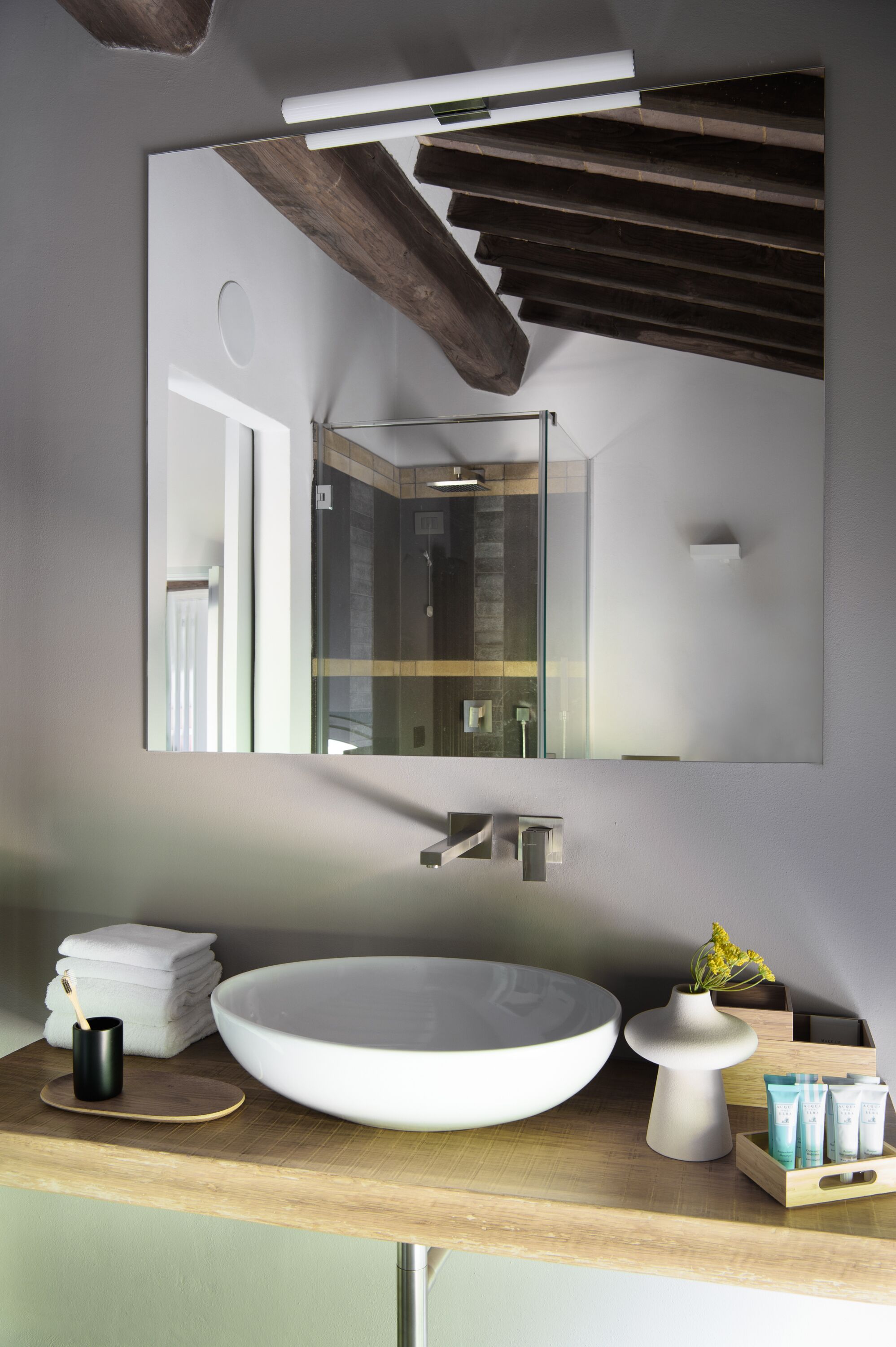 Un baño moderno con un lavamanos ovalado grande, un espejo y un techo de madera.