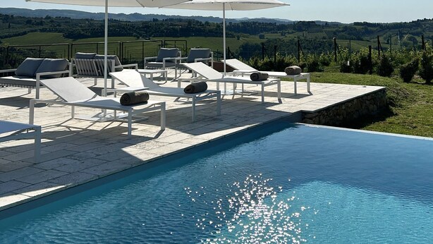 Zona de piscina con sillones y sombrillas, con vistas a un paisaje pintoresco.