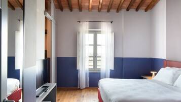Una camera d'albergo con un letto, una televisione, una finestra con tende e un soffitto in legno.