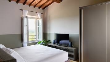 A bedroom with a bed, a TV on a stand, a window with curtains, and a door.