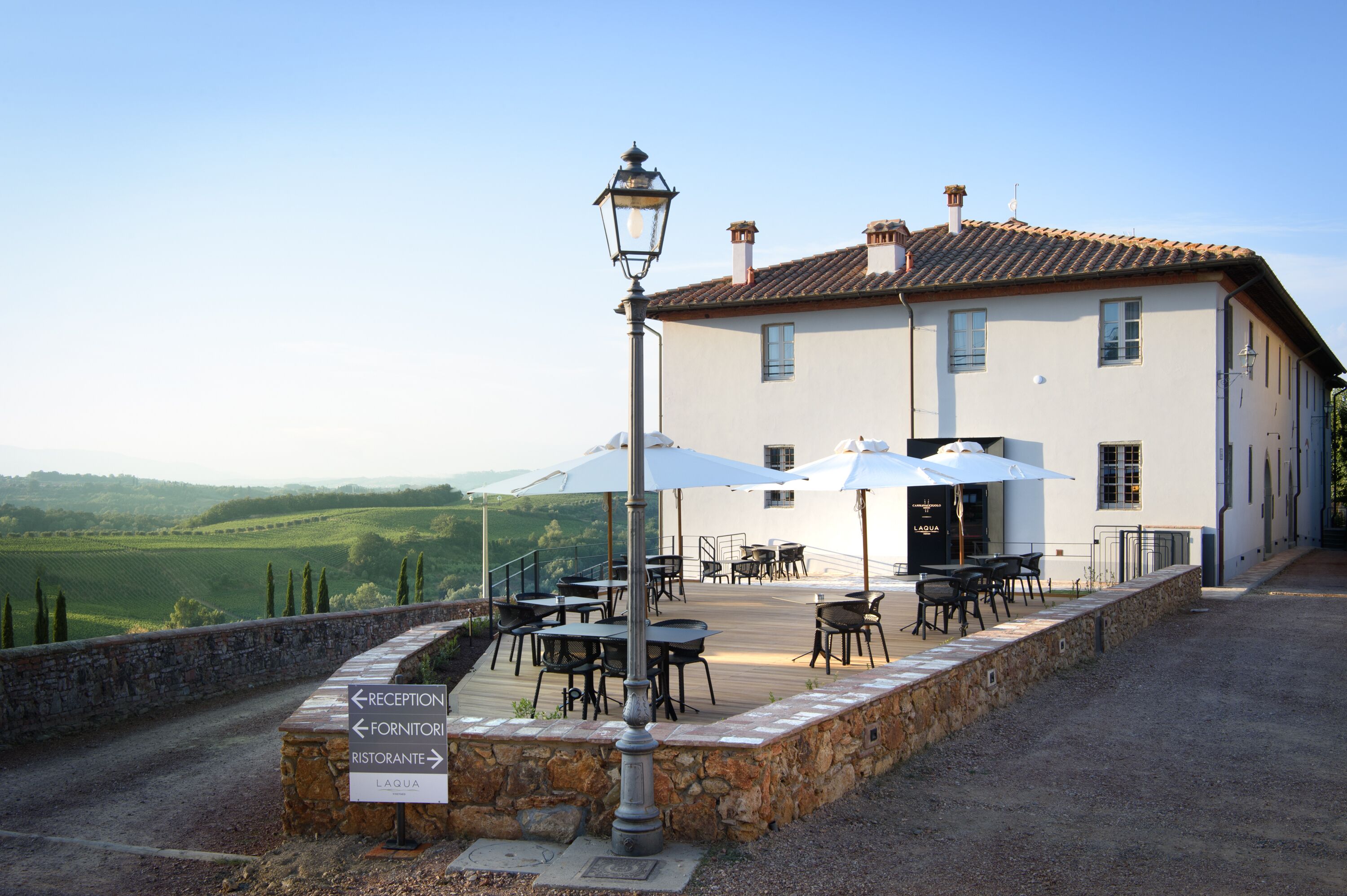 A white building with a terrace, outdoor tables, and chairs, and a sign indicating reception, restaurant, and laqua.