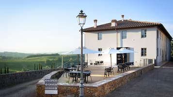 A white building with a terrace, outdoor tables, and chairs, and a sign indicating reception, restaurant, and laqua.