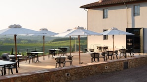 Un patio al aire libre con mesas y sillas, sombrillas y vistas al campo.