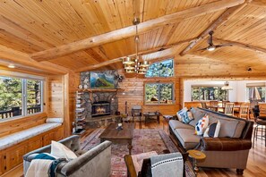 A log cabin interior with a fireplace, seating area, and large windows.