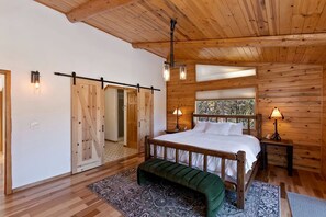 A wooden cabin bedroom with a bed, bench, and two wall-mounted lamps. - Sky Pine Retreat by Destination Big Bear: Log Cabin Home! Game Room! HOT TUB! EV Charger! (Big Bear Lake)