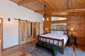 Quarto de cabana de madeira com cama, um banco e duas luminárias de cabeceira.