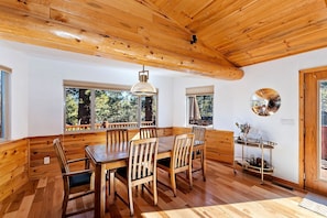 A wooden dining area with a large table and chairs, a hanging light fixture, and a small cart with items. - Sky Pine Retreat by Destination Big Bear: Log Cabin Home! Game Room! HOT TUB! EV Charger! (Big Bear Lake)