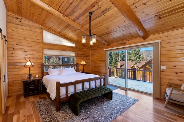 A wooden cabin bedroom with a bed, bedside tables, a bench, and a large sliding glass door leading to an outdoor area.