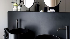 Un baño moderno con tocador negro, dos lavamanos, un espejo grande y una lámpara en el techo.