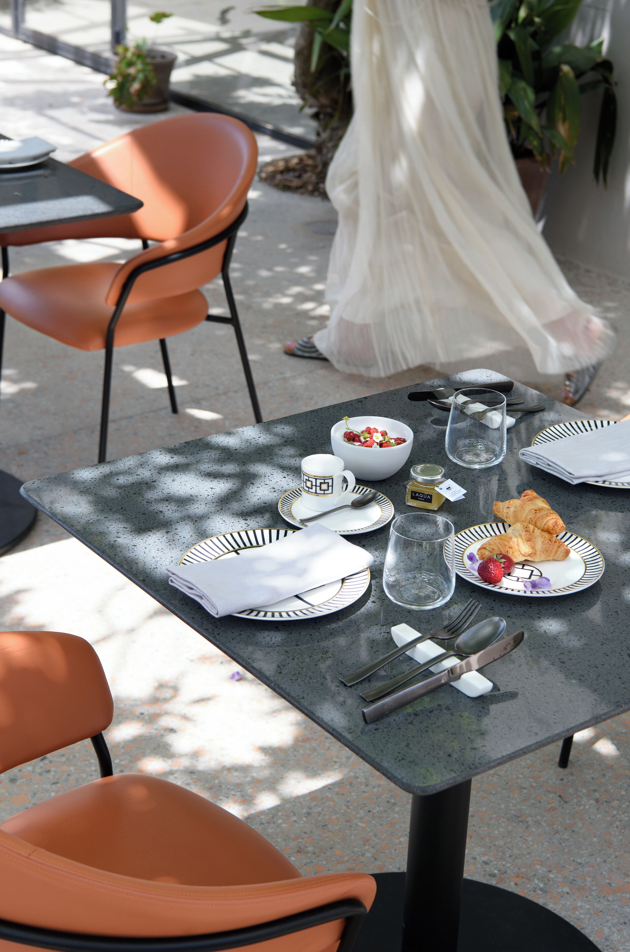 Een gedekte tafel met borden, bestek, een glas en een croissant.