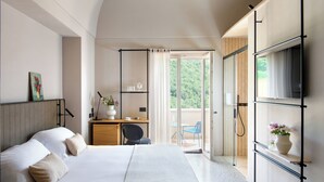 Un dormitorio con cama, un escritorio con silla, un televisor montado en la pared y un ventanal corredizo que da a un balcón.